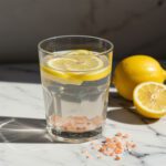 Fresh detox water made with lemon slices and pink Himalayan salt on a white marble surface.