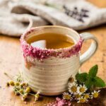 Pink salt calming tisane in a ceramic mug with herbs and crystals.