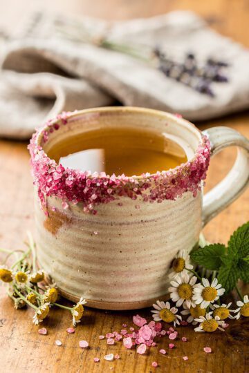 Pink salt calming tisane in a ceramic mug with herbs and crystals.