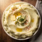 Creamy mashed potatoes with pink salt in a white ceramic bowl on rustic table.