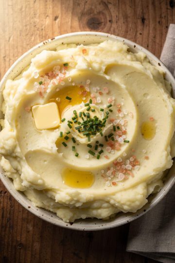 Creamy mashed potatoes with pink salt in a white ceramic bowl on rustic table.