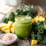 Green smoothie with kale and pineapple in a jar on a rustic table.