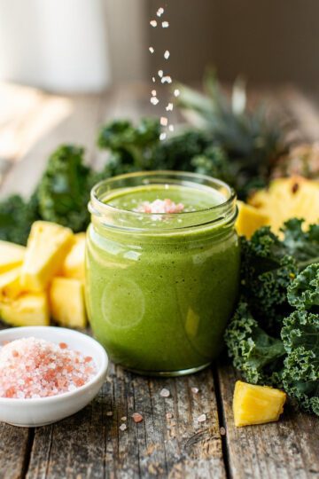 Green smoothie with kale and pineapple in a jar on a rustic table.