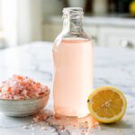 Pink Himalayan salt electrolyte concentrate in a clear glass bottle with lemon slices