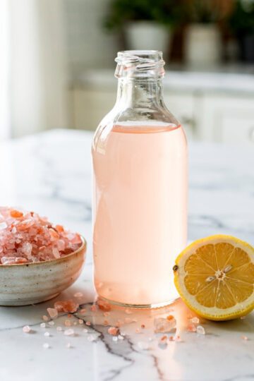 Pink Himalayan salt electrolyte concentrate in a clear glass bottle with lemon slices