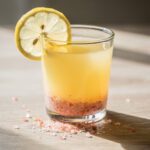 Pink salt citrus wake up shot in glass with lemon wedge and salt crystals.