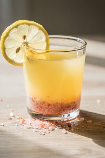 Pink salt citrus wake up shot in glass with lemon wedge and salt crystals.
