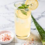 Pink salt lemon aloe refresher in a clear glass with ice and lemon slices.