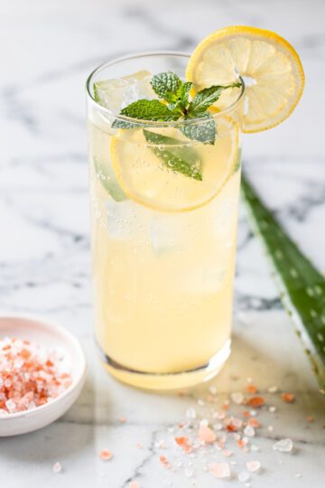 Pink salt lemon aloe refresher in a clear glass with ice and lemon slices.