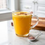 Golden milk latte in clear mug on white marble countertop