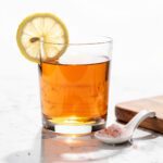 Warm amber liquid with lemon in sleek glass on marble.