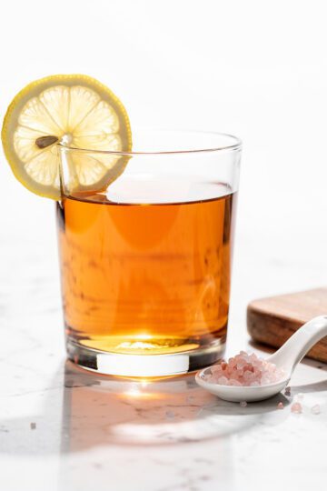 Warm amber liquid with lemon in sleek glass on marble.