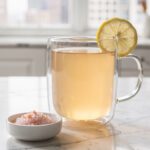 Glass of warm lemon water with salt on marble countertop.