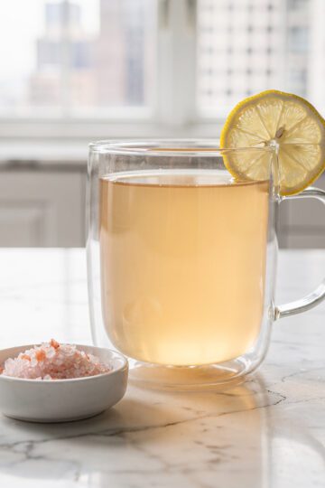 Glass of warm lemon water with salt on marble countertop.