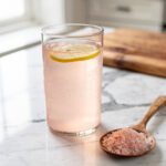 Pink Himalayan salt electrolyte drink with lemon on marble countertop